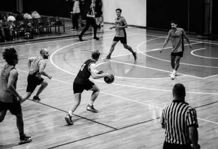 Players bringing the ball up the court while a referee watches